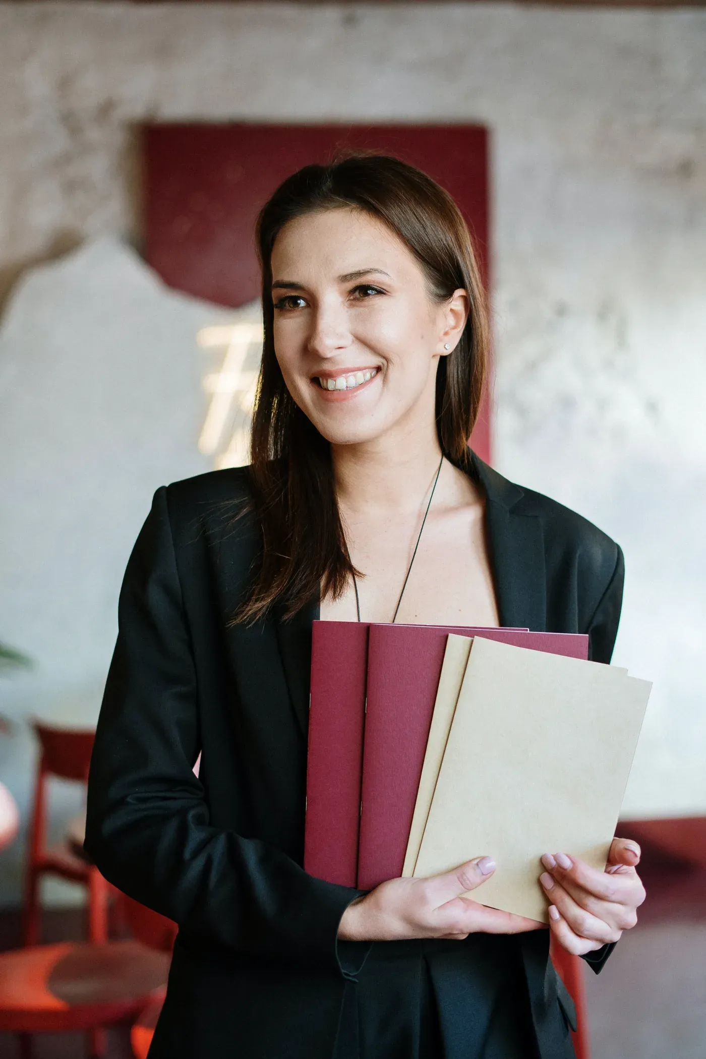 Smiling woman in a black blazer holding menus in a restaurant